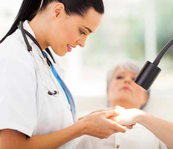Friendly dermatologist examining senior woman's skin under light