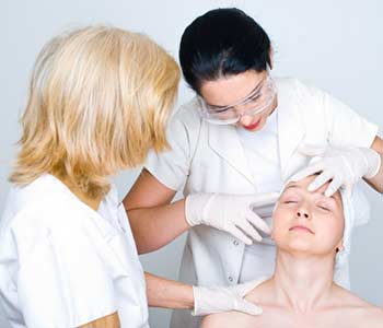 Two doctors women consulting a patient woman skin and the young doctor pointing and showing something on patient face to her colleague